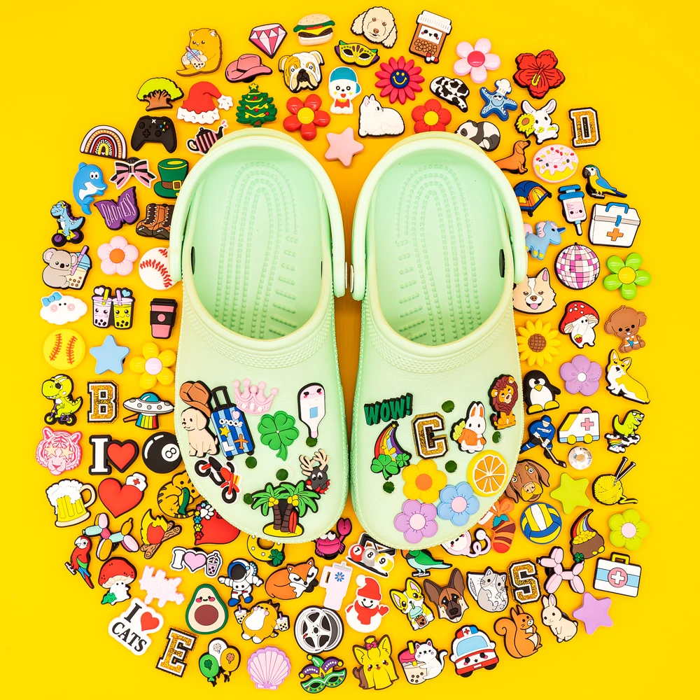 20/50/100pcs kawaii shoe charms with cartoon animals, hearts, rainbows, food, flowers and pastel icons displayed on green clogs and yellow background