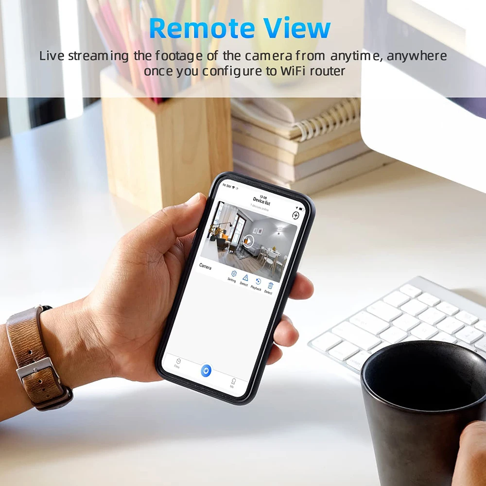 A person's hand holding a smartphone displaying a live security camera feed, with a text overlay "remote view" at a desk with a coffee cup and a SpyCam Clock to monitor surroundings.