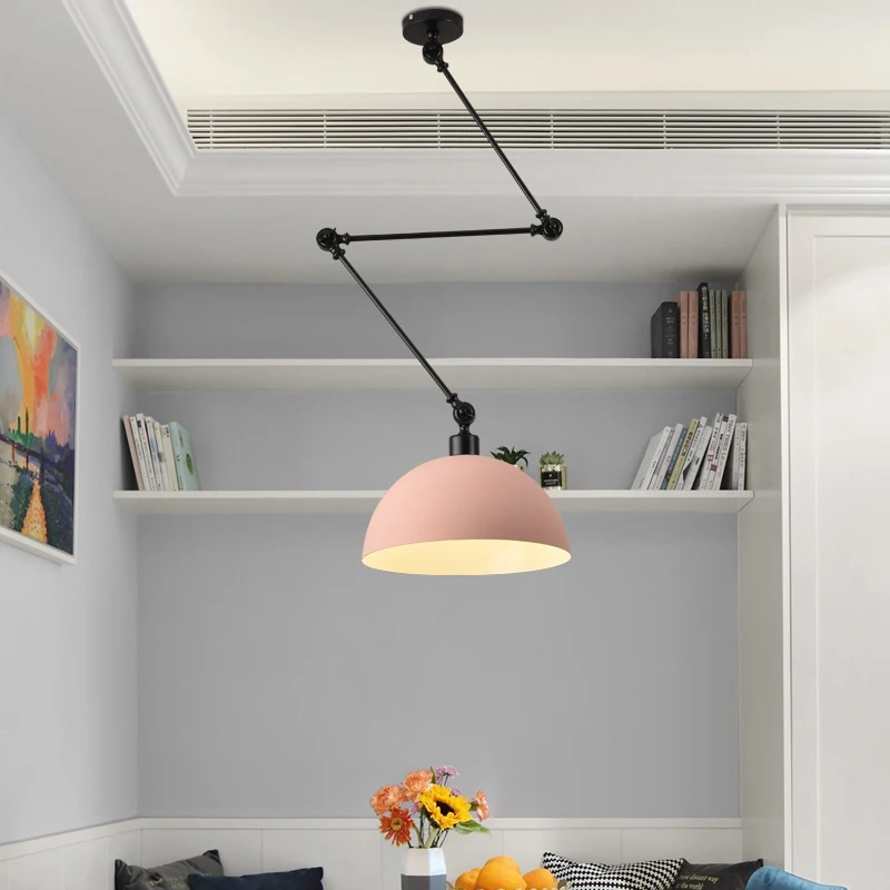 A Zig Zag Pendant Light with a pink shade hangs in a room with light gray walls. Bookshelves and a decorative vase are in the background, while a table below is embellished with a bouquet of flowers for added charm.