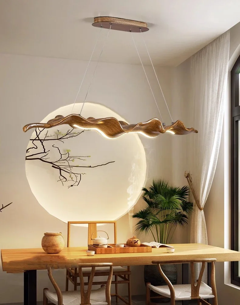Modern dining room with a wooden table, chairs, and the Leaf Pendant Light featuring textured surface lighting. A large circular wall decoration and potted plants in neutral beige tones enhance the decor.
