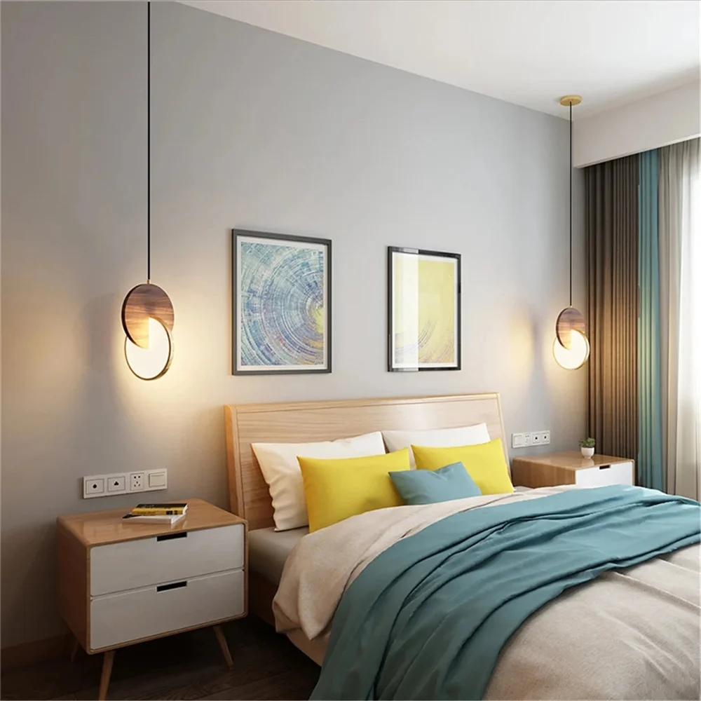 A minimalist bedroom showcasing a wooden bed with elegant blue and yellow bedding, two bedside tables, modernist lighting from a Dual Disc Pendant Light, and framed abstract art on the wall.