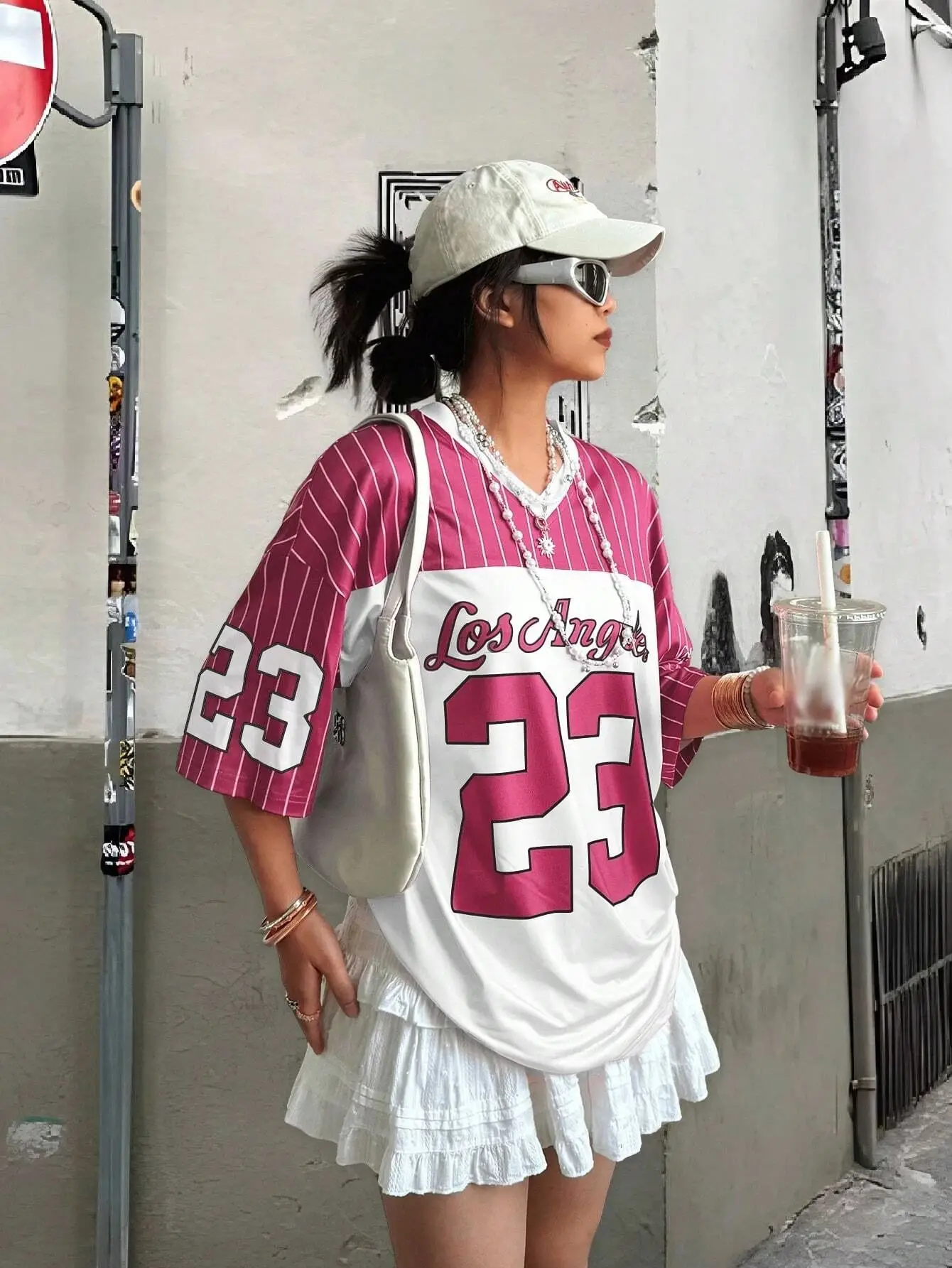 Man and woman wearing matching short-sleeved V-neck T-shirts with bold “23” digital print, standing in a sunny urban setting with sporty accessories pink