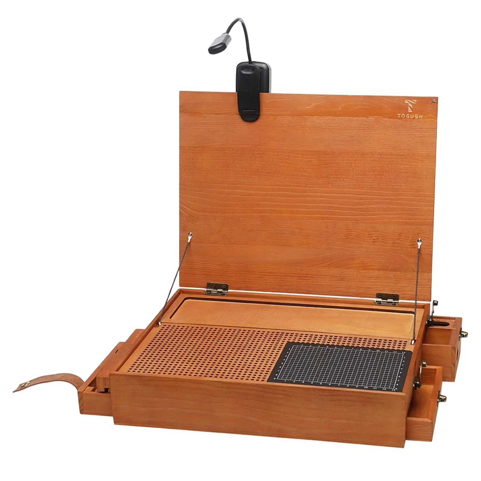Détail du tapis de découpe quadrillé sur l'établi pliable, avec un cutter posé à côté.