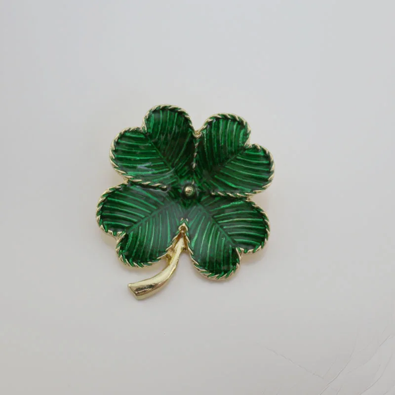 Green four-leaf clover brooch with gold trim on a light gray background