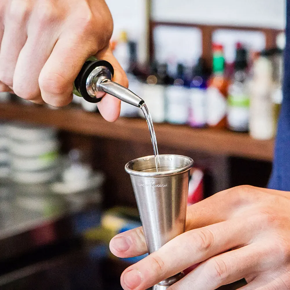 Bartender Holds In Hand Steel Jigger And Pours Drink From Bottle