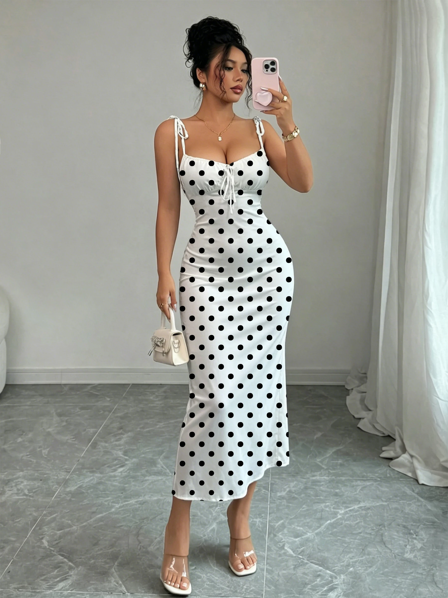 Robe sirène noire à pois sur fond blanc, avec double nœud papillon aux épaules et fronces sur la poitrine pour une mise en valeur de la taille, coupe ajustée, moulante aux hanches, longueur mi-longue