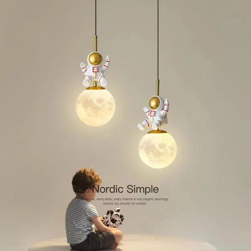 A little boy is playing with a robot under two moon floating hanging lights.