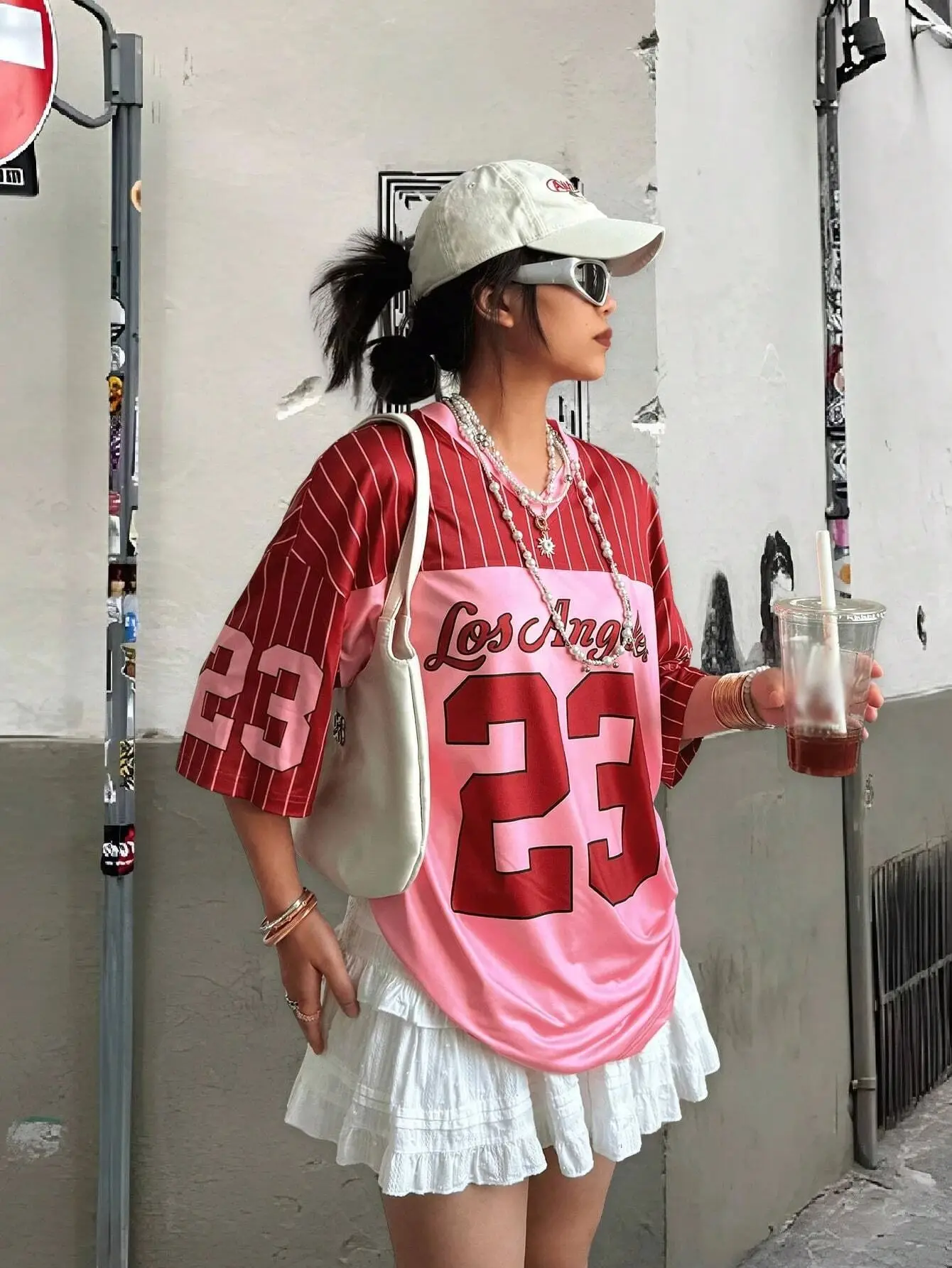 Man and woman wearing matching short-sleeved V-neck T-shirts with bold “23” digital print, standing in a sunny urban setting with sporty accessories red