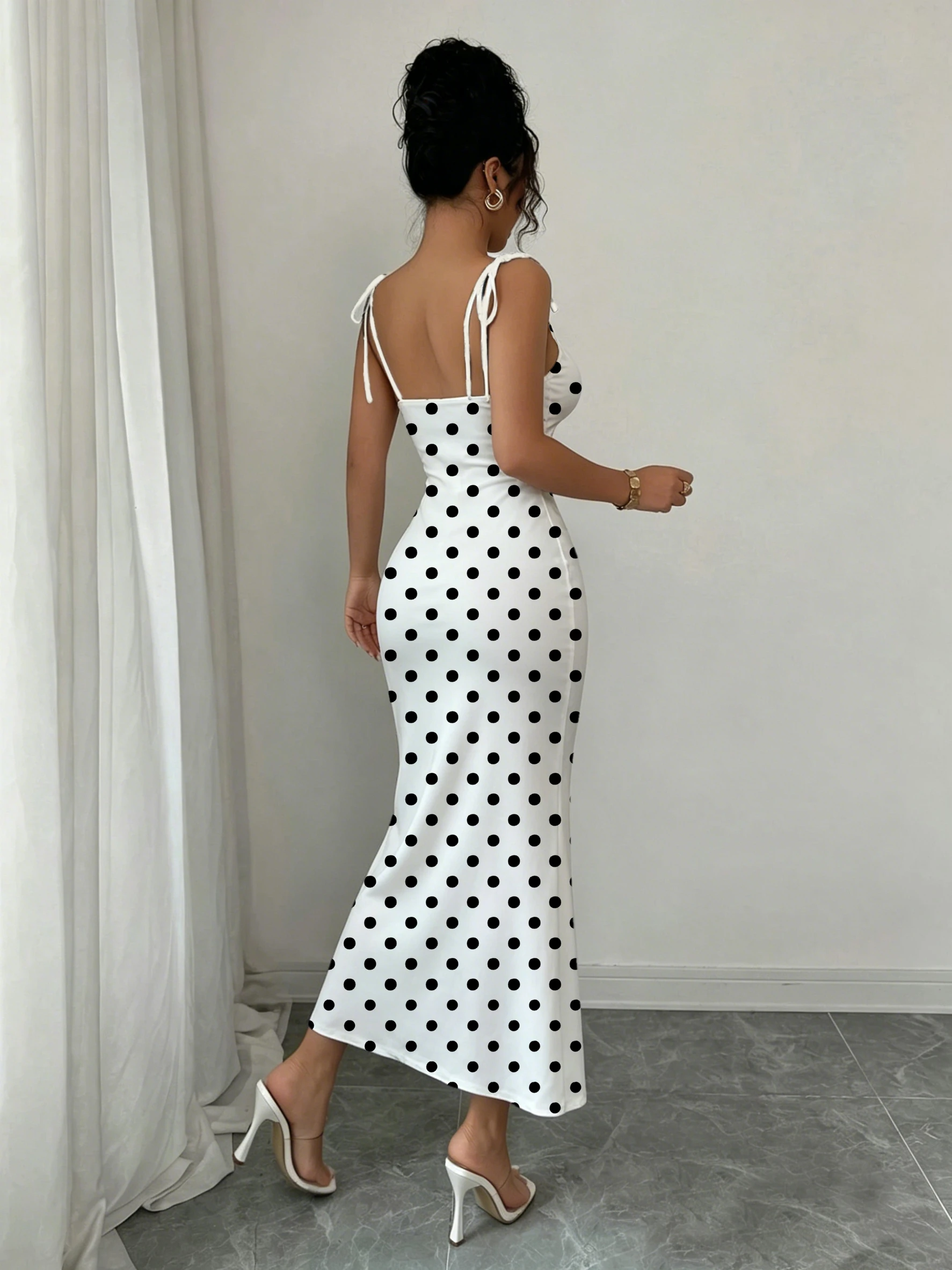 Robe sirène noire à pois sur fond blanc, avec double nœud papillon aux épaules et fronces sur la poitrine pour une mise en valeur de la taille, coupe ajustée, moulante aux hanches, longueur mi-longue
