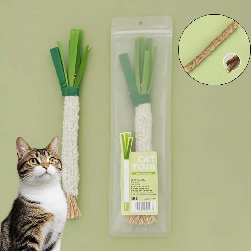 A cat eyes The Ultimate Kitten Teething Wand Toy by KittyNook Cat Co., shaped like a green veggie with a wood stick.