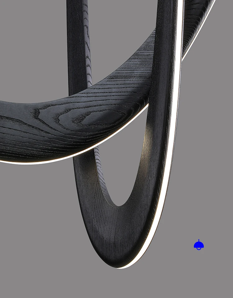 Close-up of intersecting black wooden rings with lit edges from the Double Curve Wood Pendant Light against a gray background; a small blue object is visible near the bottom right corner.