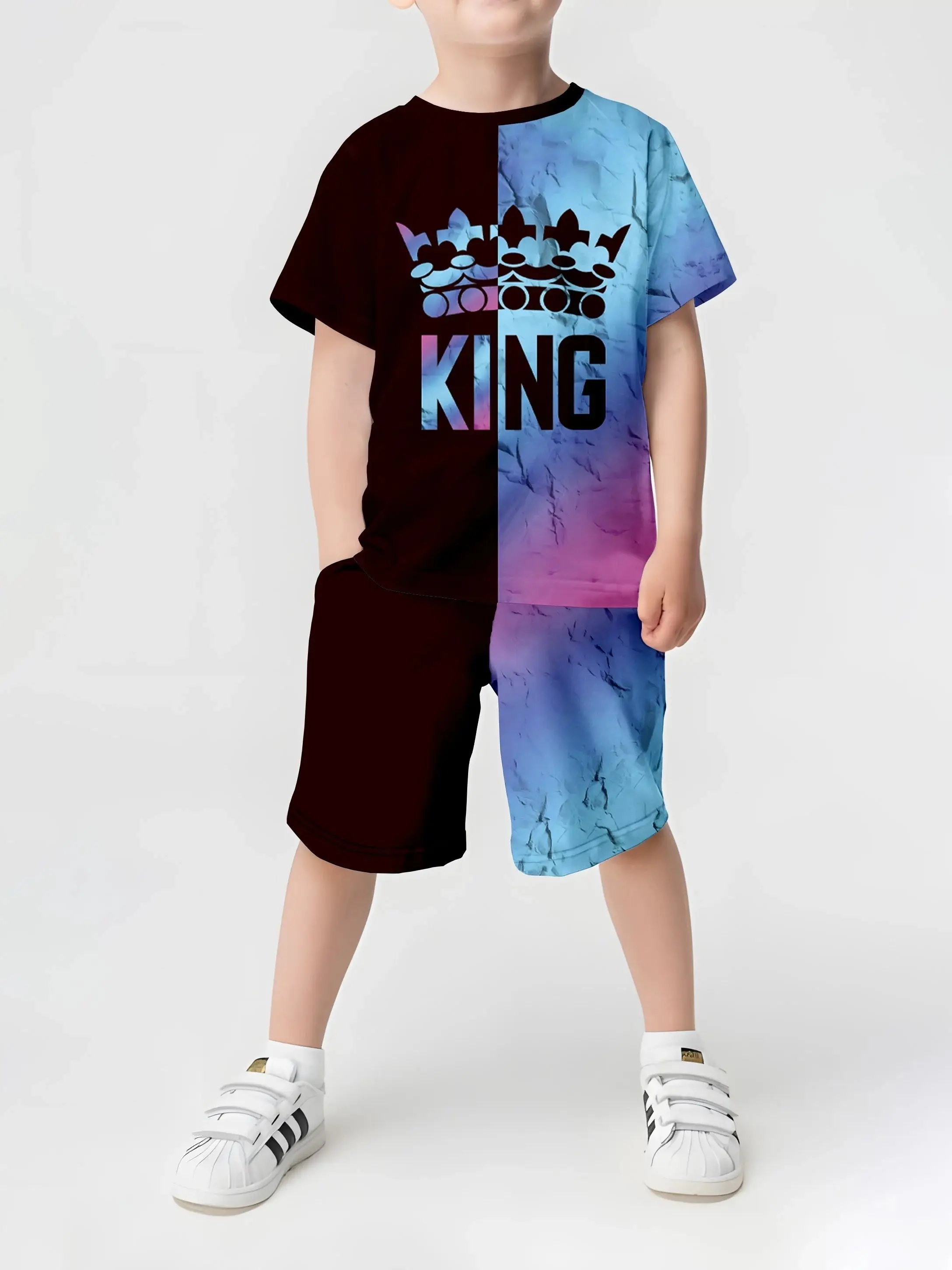 Child wearing a short sleeve crown-printed T-shirt and matching shorts, smiling outdoors in a sunny park with playful energy blue