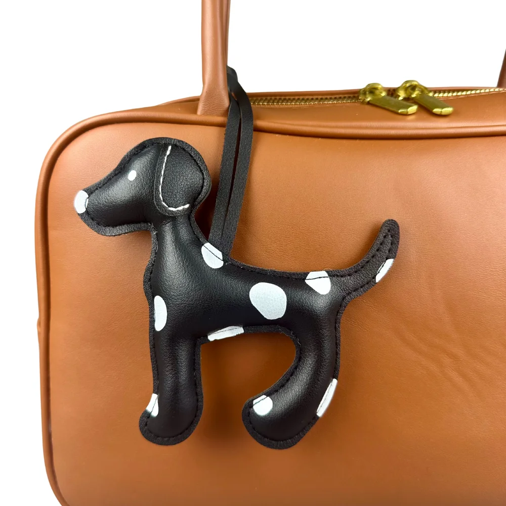 A crisp white PU leather Dalmatian dog bag charm with black spots hanging elegantly from the handle of a navy blue leather purse.