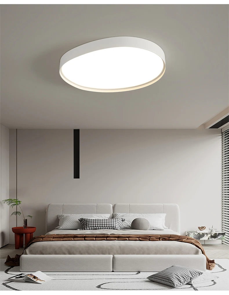 A modern bedroom with a minimalist white bed illuminated by a sleek round ceiling light.