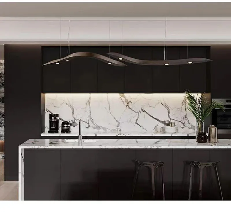 Modern kitchen with dark cabinets, marble backsplash and countertop, a Spiral Wood Pendant Light, bar stools, a sink, coffee machine, and decorative plants on the island.