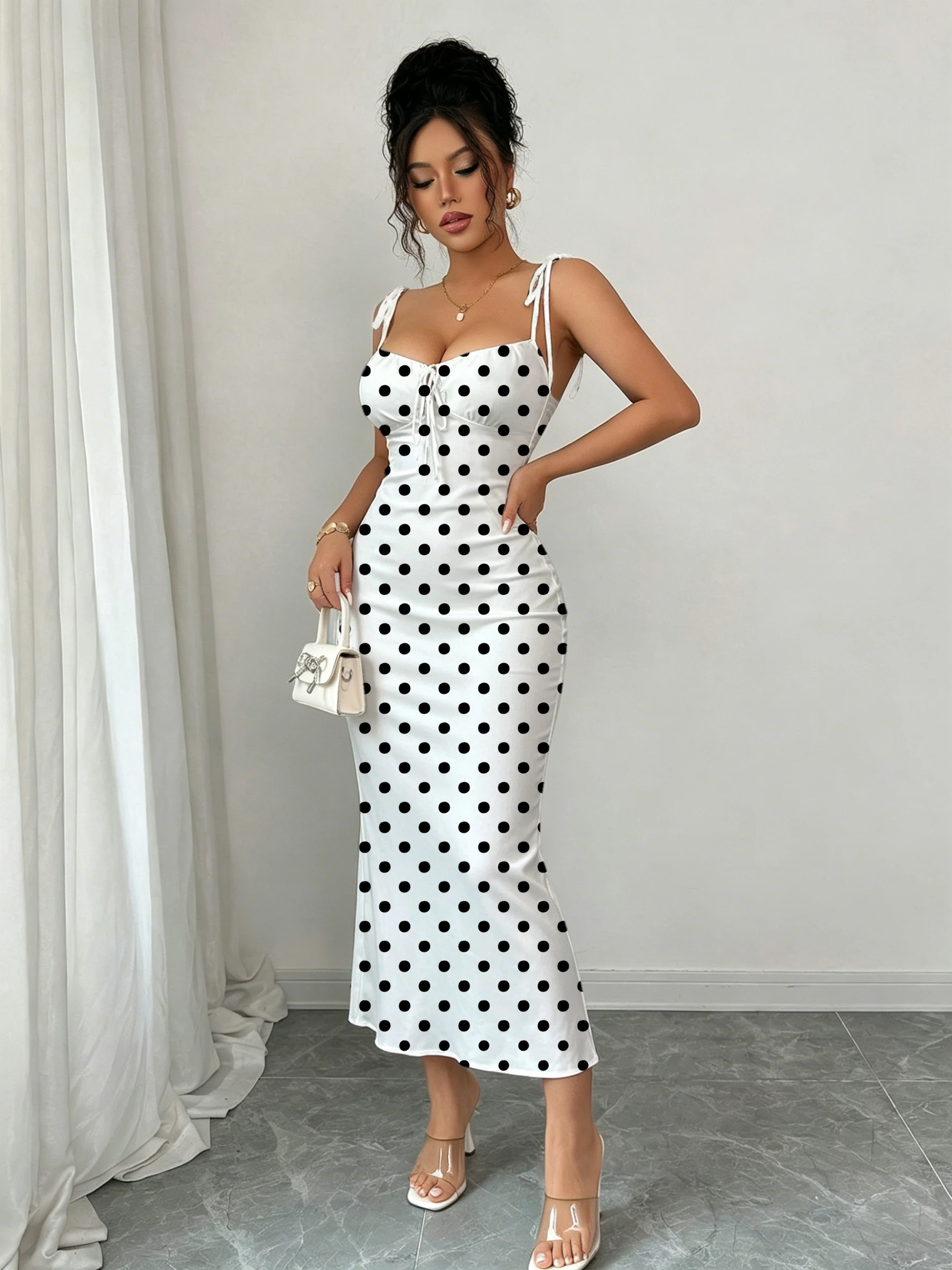 Robe sirène noire à pois sur fond blanc, avec double nœud papillon aux épaules et fronces sur la poitrine pour une mise en valeur de la taille, coupe ajustée, moulante aux hanches, longueur mi-longue