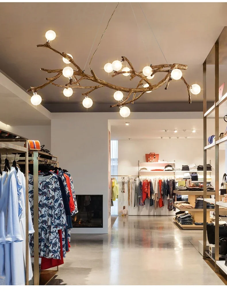 The clothing store interior is illuminated by the Branch Pendant Light, featuring glass orb shades reminiscent of tree branches. Clothing racks and shelves line the walls, blending style and functionality with this organic modern lighting centerpiece.
