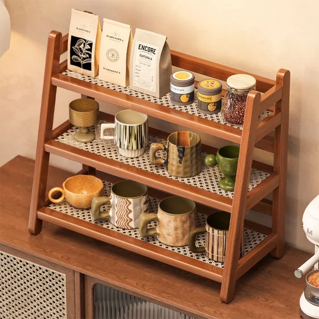 A 3-tier bamboo shelf organizer sitting on a kitchen counter, neatly arranged with white coffee mugs, a sugar bowl, and a small plant.