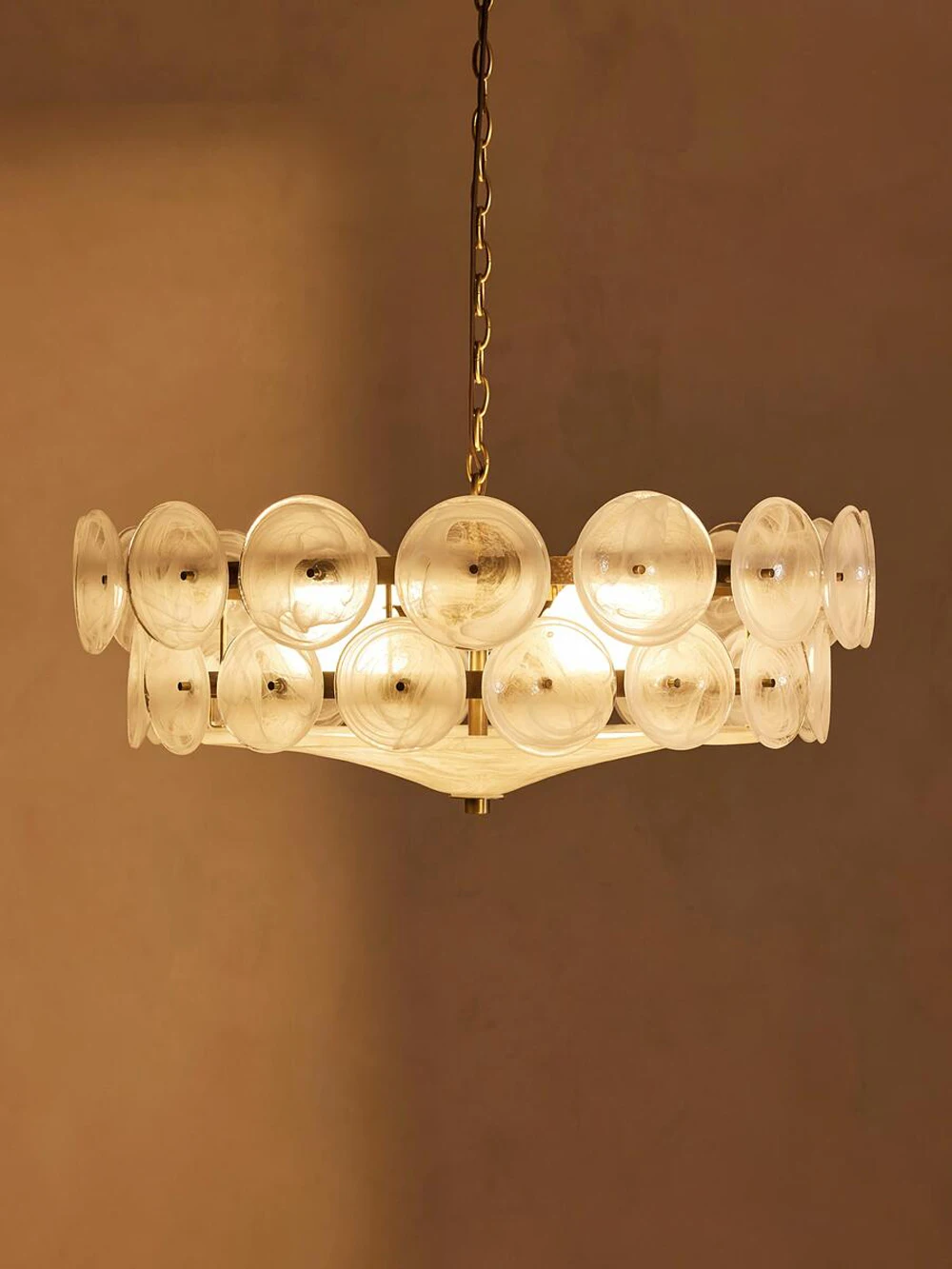 The Italian Retro Pendant Light showcases round, translucent Murano glass discs with warm lighting, hanging from a gold chain against a beige wall.
