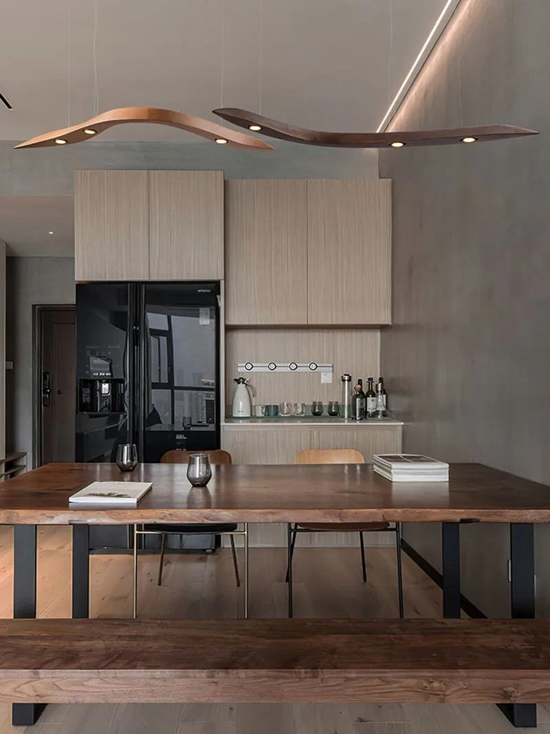 Modern minimalist kitchen with light wood cabinets, a black refrigerator, and a wooden dining table with bench seating, featuring two Spiral Wood Pendant Lights for organic modern lighting.