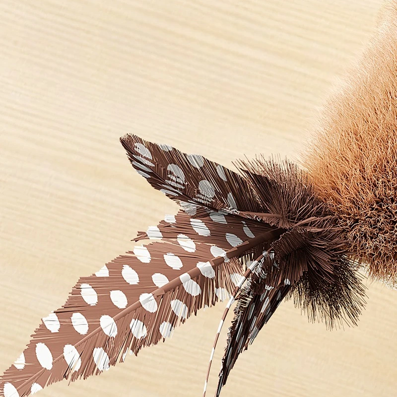 Close-up of a brown feather with white spots from the KittyNook Cat Co. Squeaky Plush Cat Toy on light wood.
