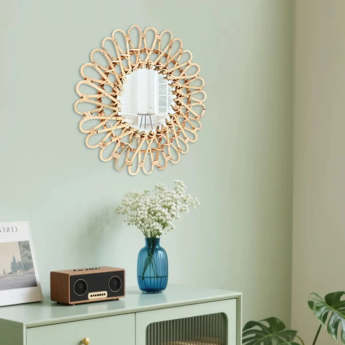 Rotan wandspiegel tegen salie-groene muur met blauwe vaas en speaker