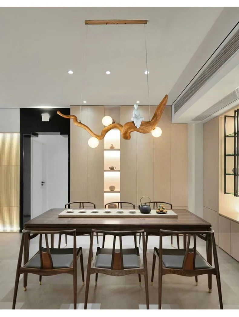 A modern dining room showcases a wooden table with six chairs, highlighted by the Zen-Inspired Wooden Pendant Light, crafted from twisted wooden branches with round bulbs. The minimalist decor is enhanced by built-in shelving in the background.