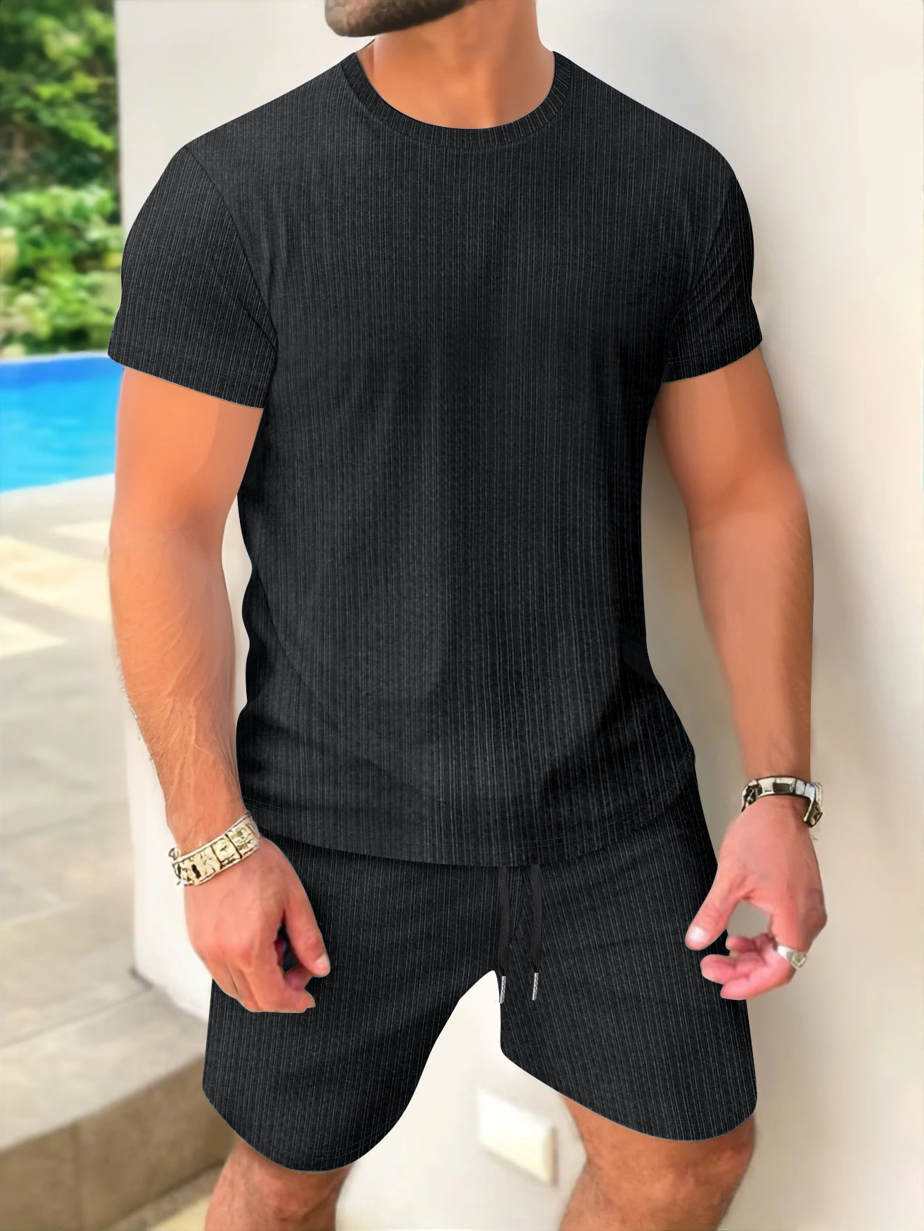 Men’s short-sleeved pullover and shorts set in solid color, styled outdoors with minimalist accessories and summer lighting black