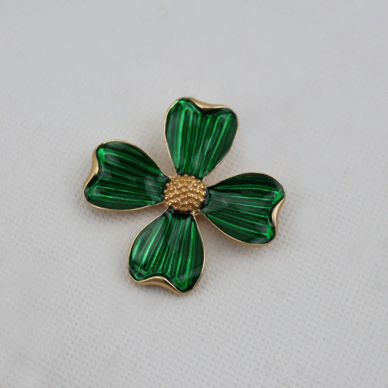 Green flower-shaped brooch with gold center on a light gray background
