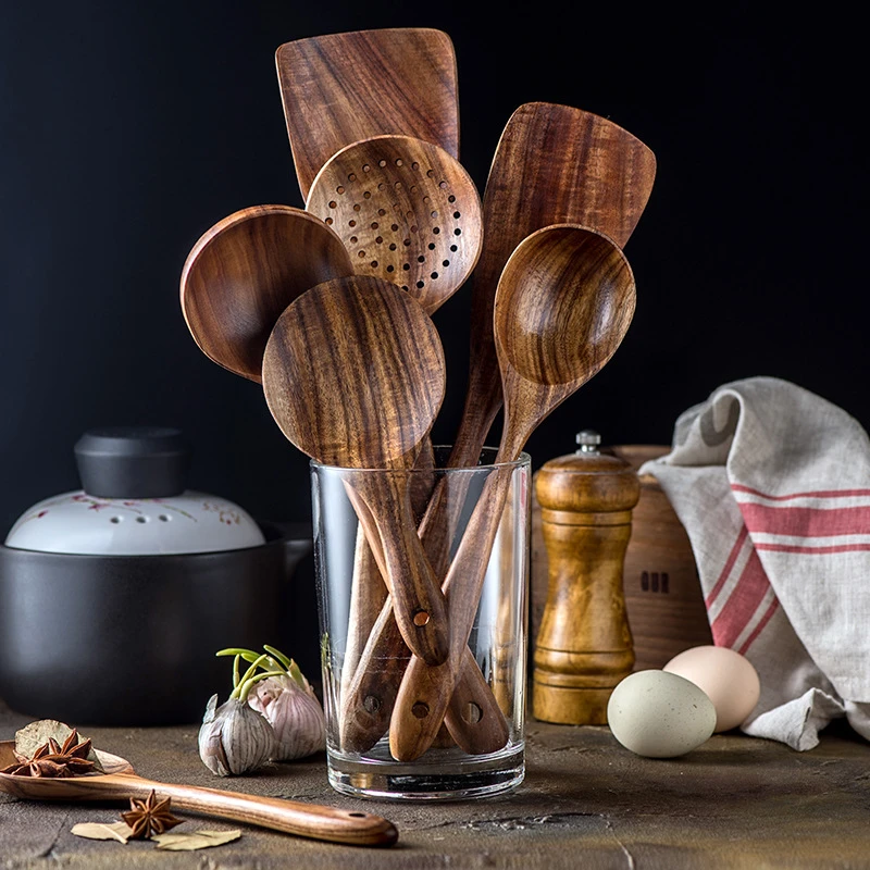 Set of natural Thailand teak wood cooking utensils including ladles, skimmers, and spoons laid out on kitchen counter 06