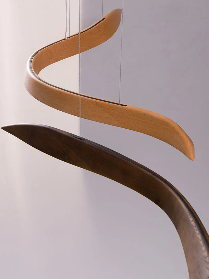 The Spiral Wood Pendant Light features two curved wooden shapes—one light, one dark—suspended by strings for an organic, modern design and artistic silhouette.