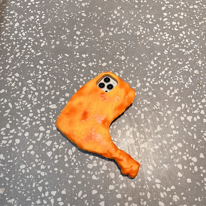 A Chicken Drumstick iPhone Case, shaped and colored like a piece of fried chicken, placed on a speckled gray surface.