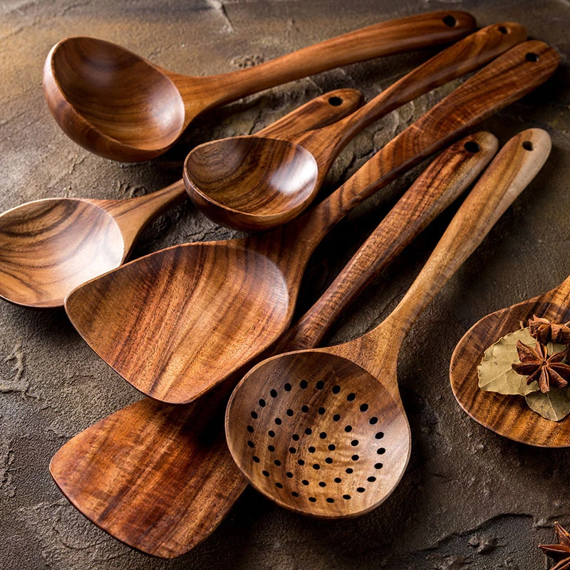 Set of natural Thailand teak wood cooking utensils including ladles, skimmers, and spoons laid out on kitchen counter  01
