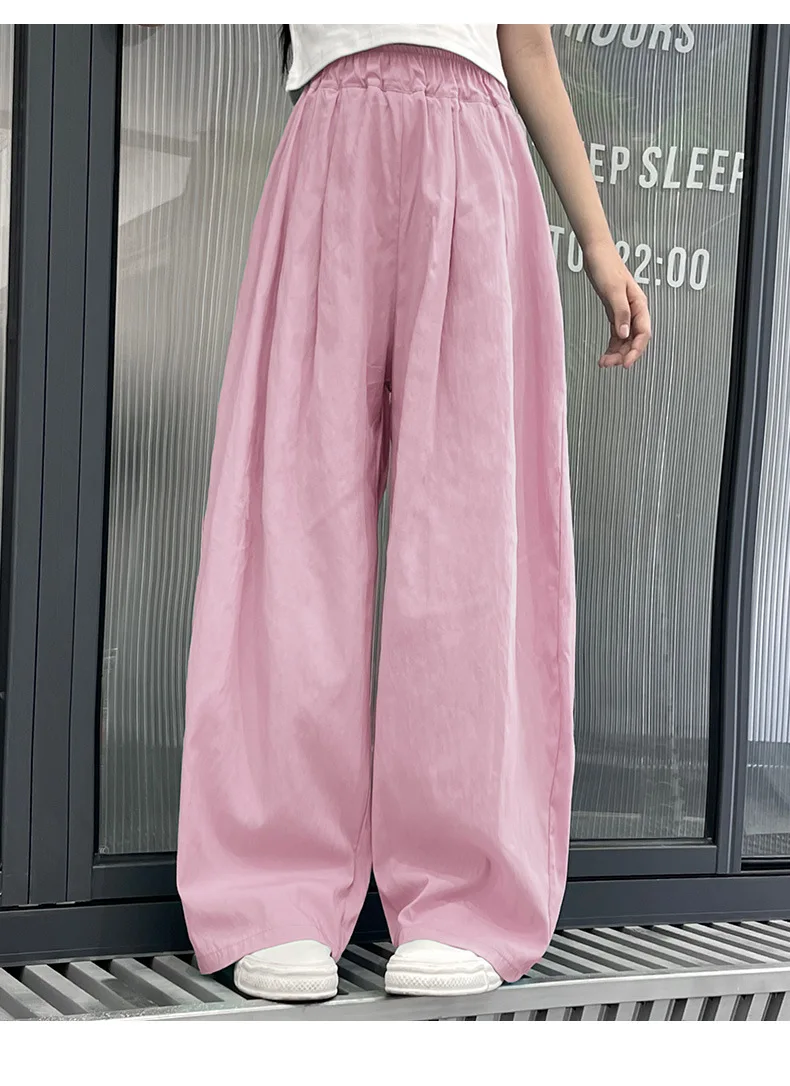 Teen girls’ casual summer wide-leg pants in lightweight fabric, styled with sandals and a simple tee on a beach boardwalk backdrop pink