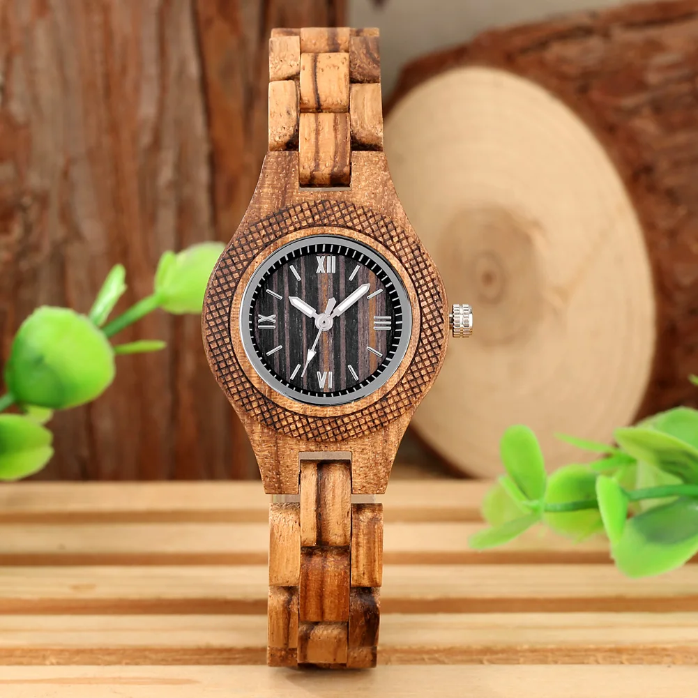 Pildil on puidust käekell naistele, millel on detailne puidust rihm ja kellaplaat. Taustal on puidust tekstuur ja rohelised lehed, mis annavad looduslähedase ja elegantse ilme.