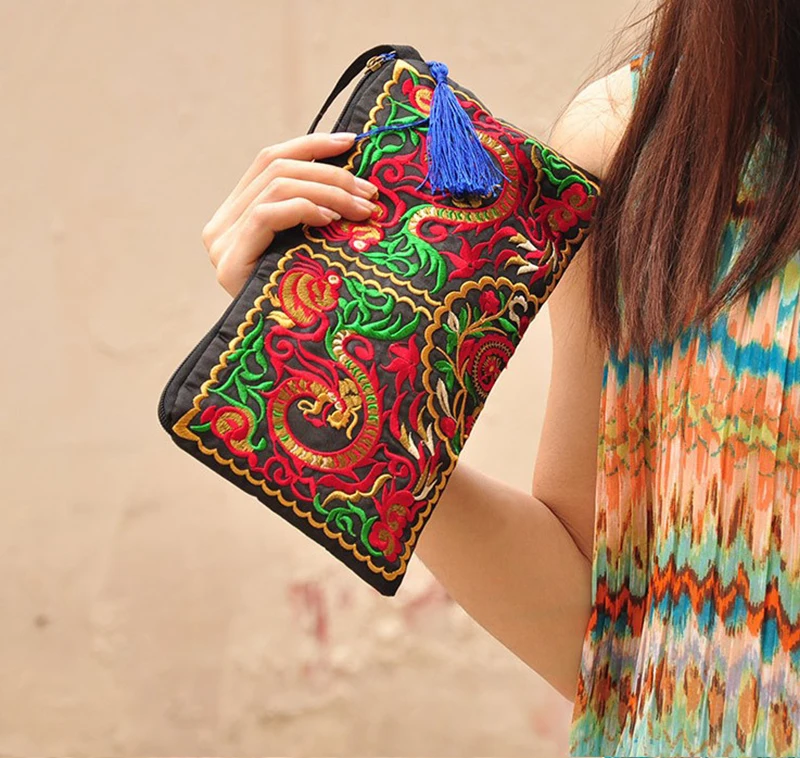 A woman is holding an Ethnic Retro Flower Clutch Bag with a tassel on it.