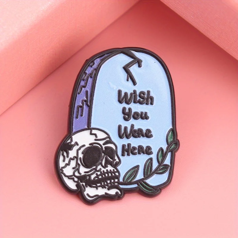 Morbid Greetings Emaille-Anstecknadel – „WISH YOU WERE HERE“, Grabstein mit rissigen Totenköpfen und grünen Akzenten, dunkler Humor-Schmuck für Friedhofs