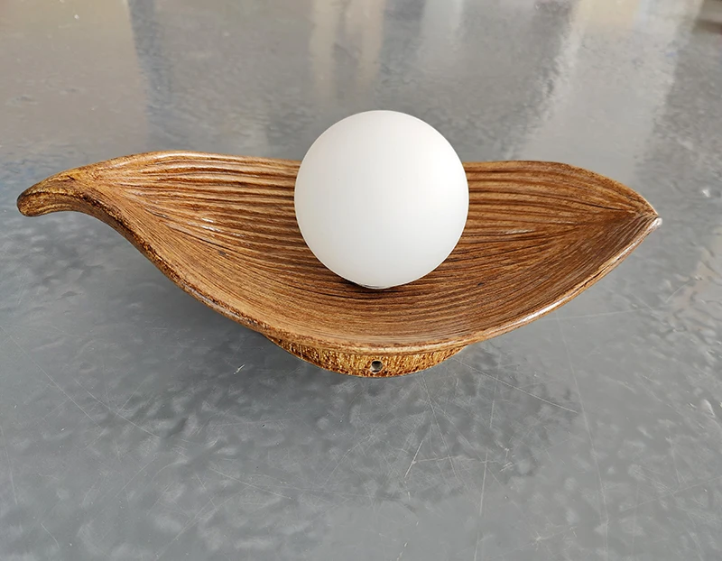 A wooden bowl with a nature-themed accent of a leaf wall light inside.