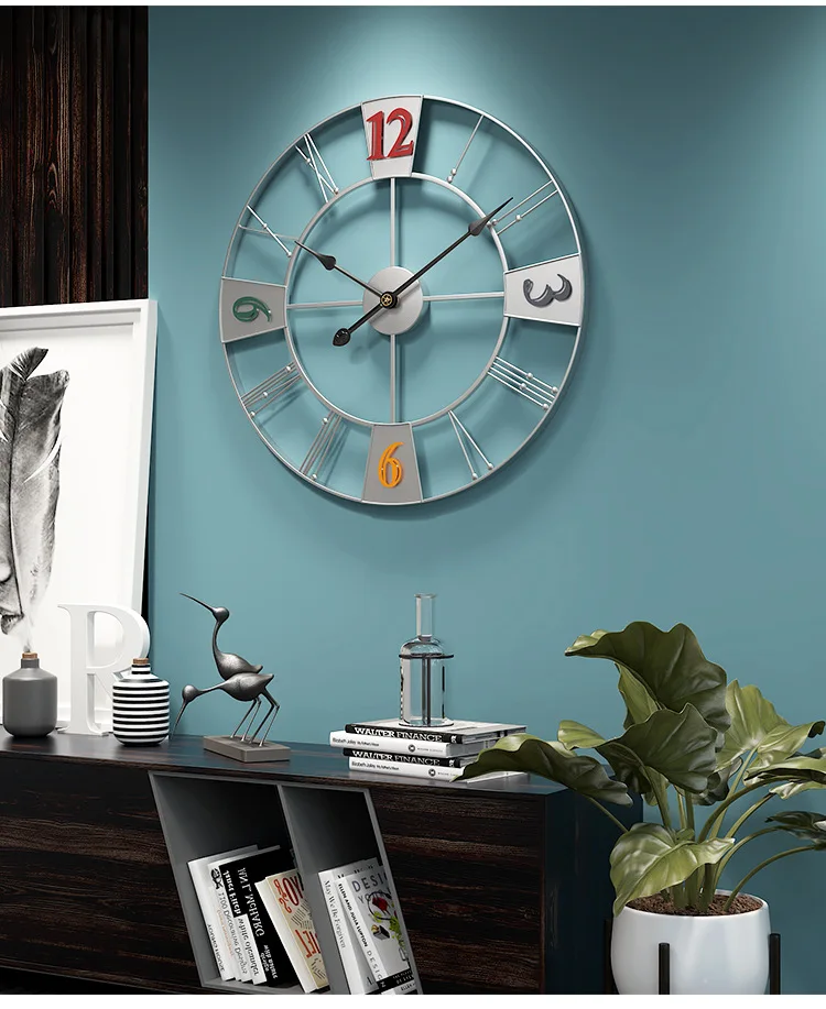A large sophisticated wall clock with Roman numeral cutouts on a blue wall above a dark wood shelf with decorative items and plants.