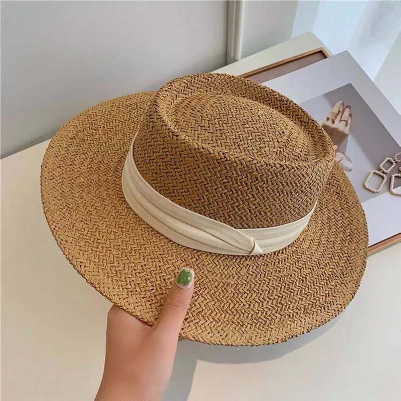 un main de femme tenant un chapeau panama en paille avec un ruban beige autour du chapeau