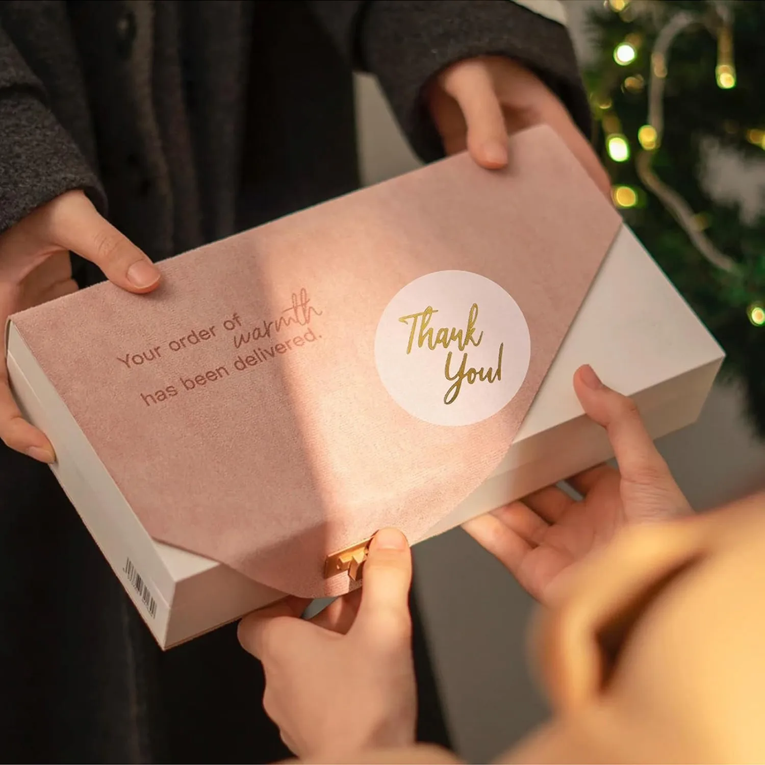 Hand applying a gold foil thank you sticker to a package