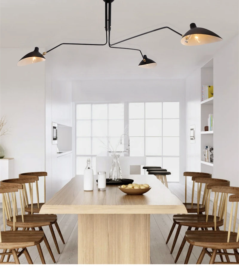 Modern dining room with a rectangular wooden table, eight chairs, and the Sleek Industrial Pendant Light featuring brass connection points. The space has large windows and minimalistic decor, complemented by a stylish black, three-arm ceiling light fixture.