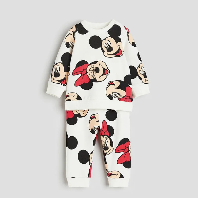 Toddler wearing a Minnie-themed sweatshirt and matching pants, smiling in a leaf-covered park with playful autumn vibes