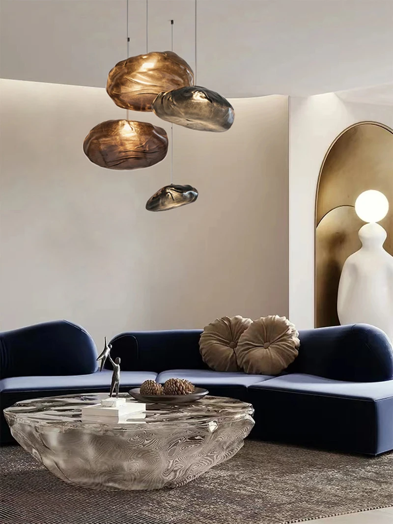 Modern living room with a blue curved sofa, sculpted glass coffee table, Luxe Cloud Glass Pendant Light cluster, and a minimalist lamp beside a gold-accented wall.