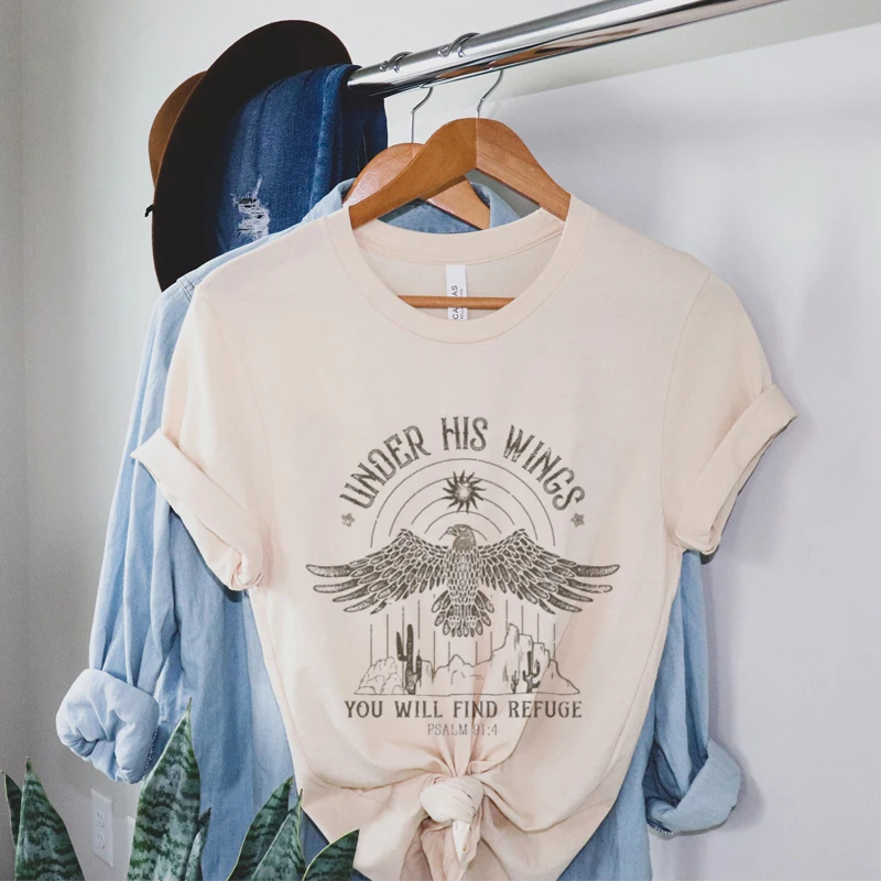 Vintage boho eagle print women's Christian t-shirt with Bible verse, faith graphic, short sleeves hanging on rack.