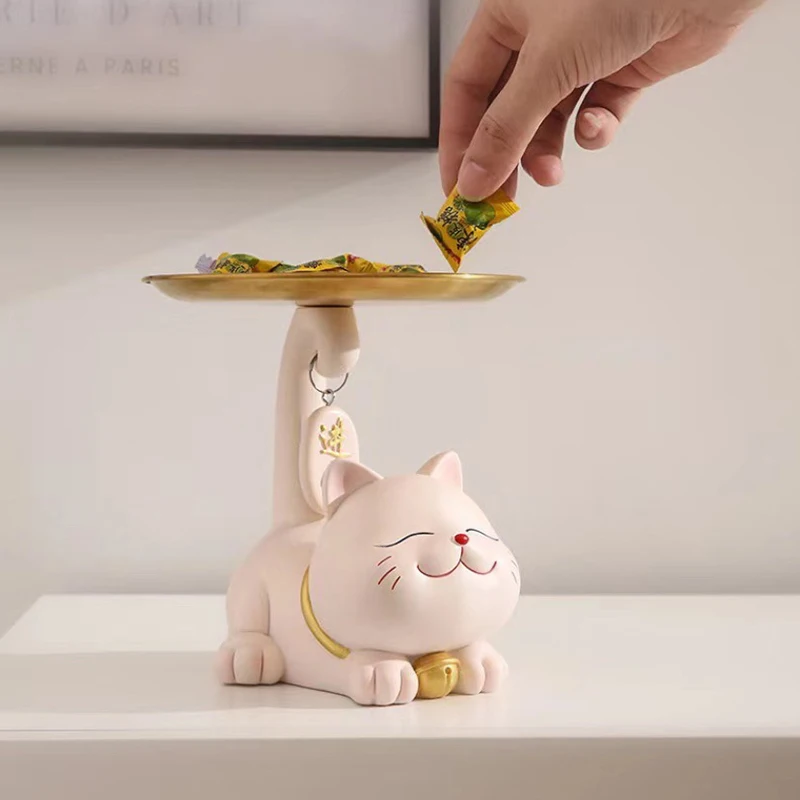 A hand places candy on the Chic Cat Metal Key Tray by KittyNook Cat Co., shaped like a smiling cat with its tail up.