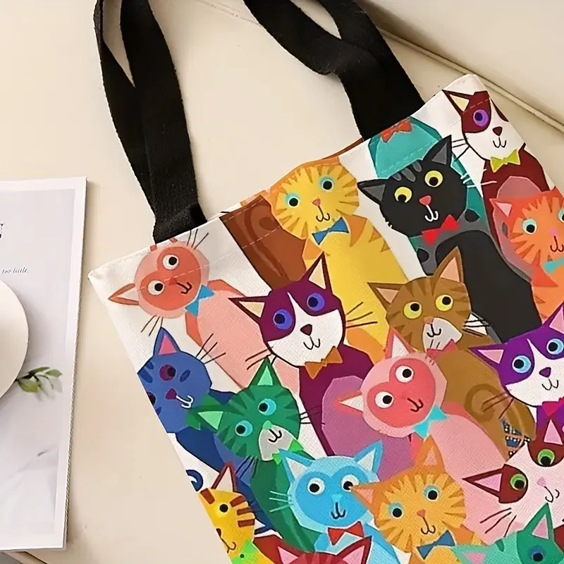 The Playful Kitten Print Canvas Handbag by KittyNook Cat Co., perfect for eco-shoppers, on a beige surface.