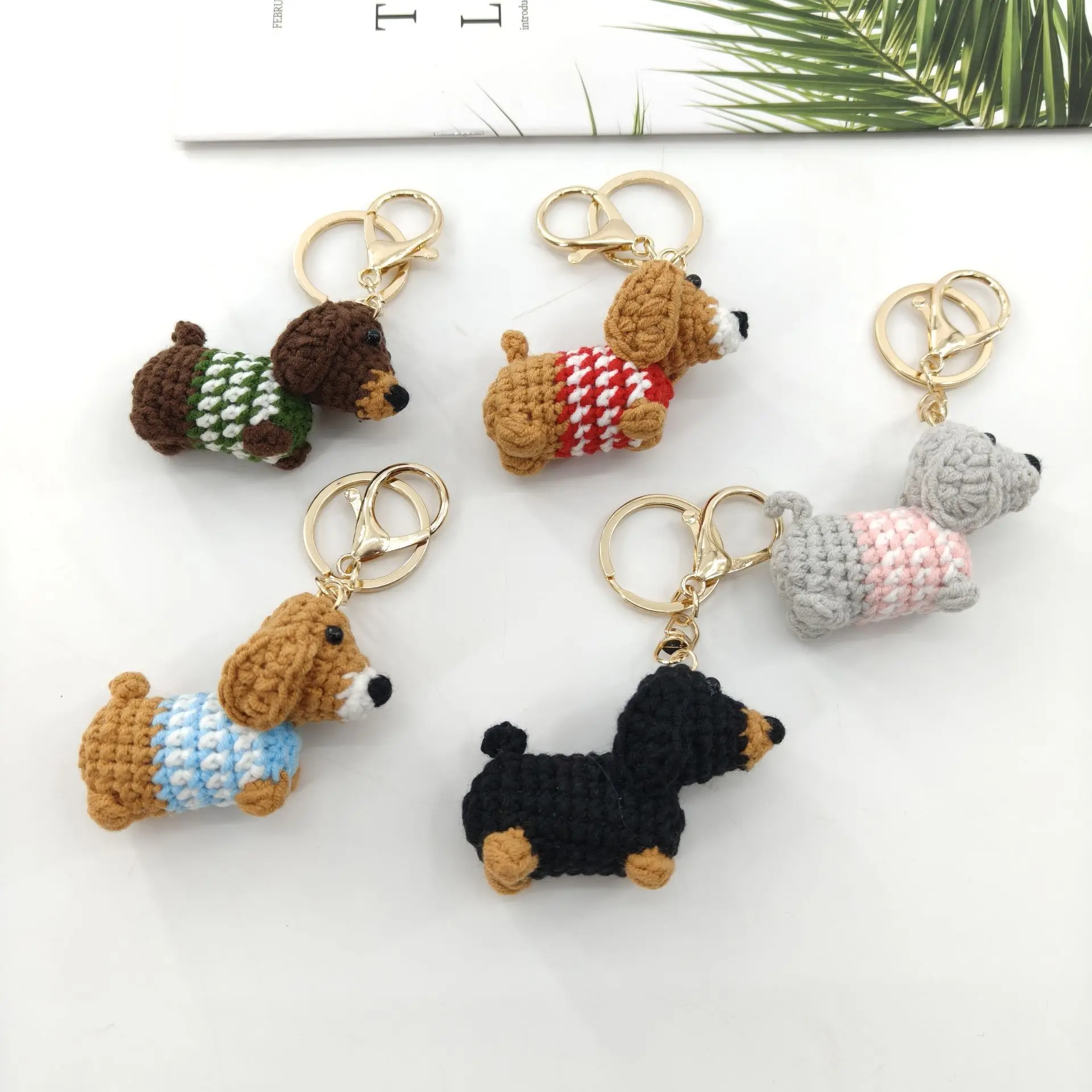 Assorted handmade crochet Dachshund dog keychains in various colors with knitted sweaters and gold carabiners.