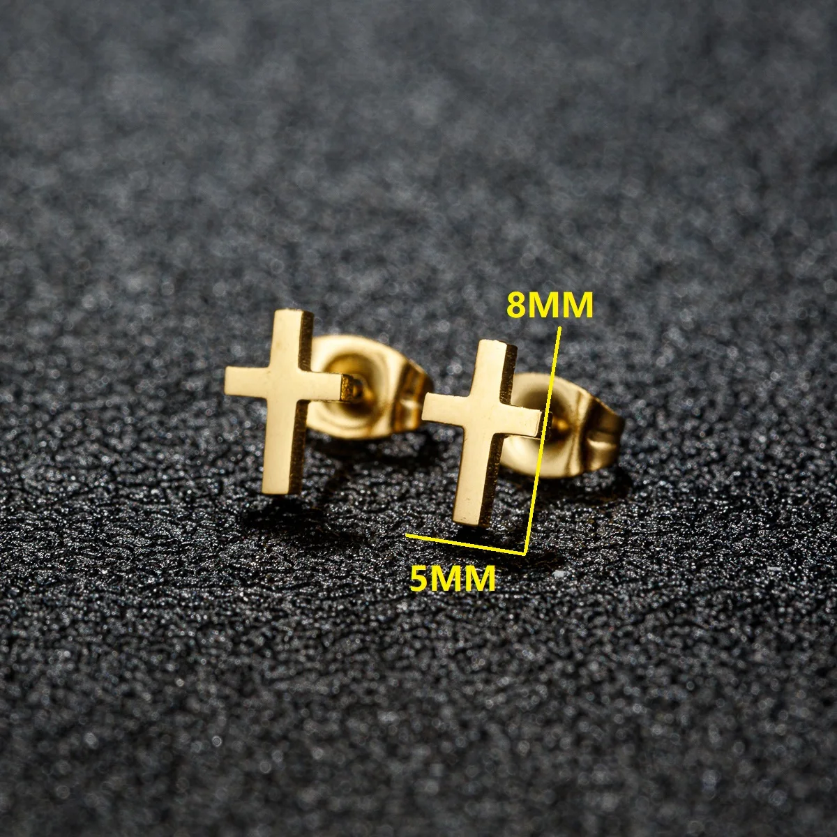 Gold tone stainless steel cross stud earrings with dimensions 8mm by 5mm displayed on a textured black surface.
