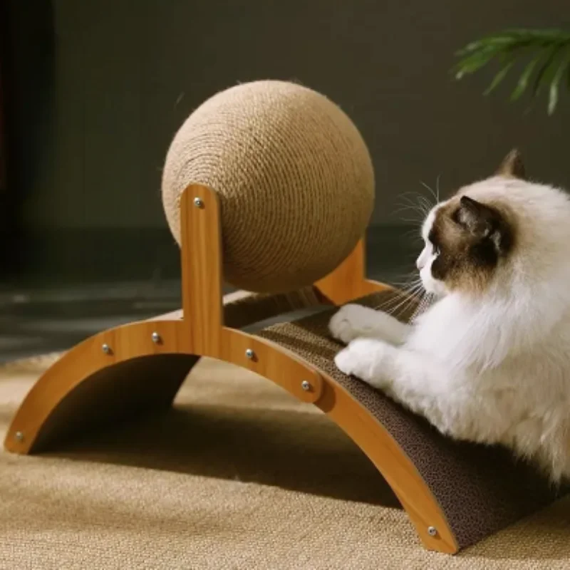 A long-haired cat is captured mid-play, using its paws to scratch the corrugated cardboard surface of the arch-shaped base while looking up at the sisal ball. The scratcher is positioned on a neutral-toned rug, illustrating its stability during use.